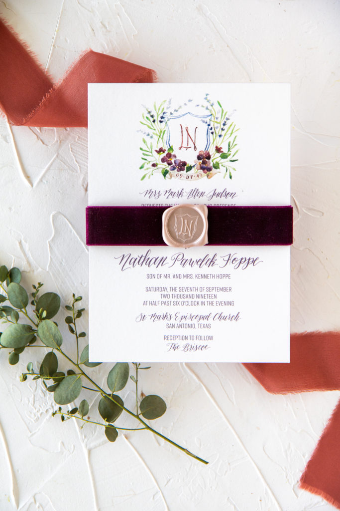 Invitation with watercolor crest and wax seal bound with velvet ribbon
